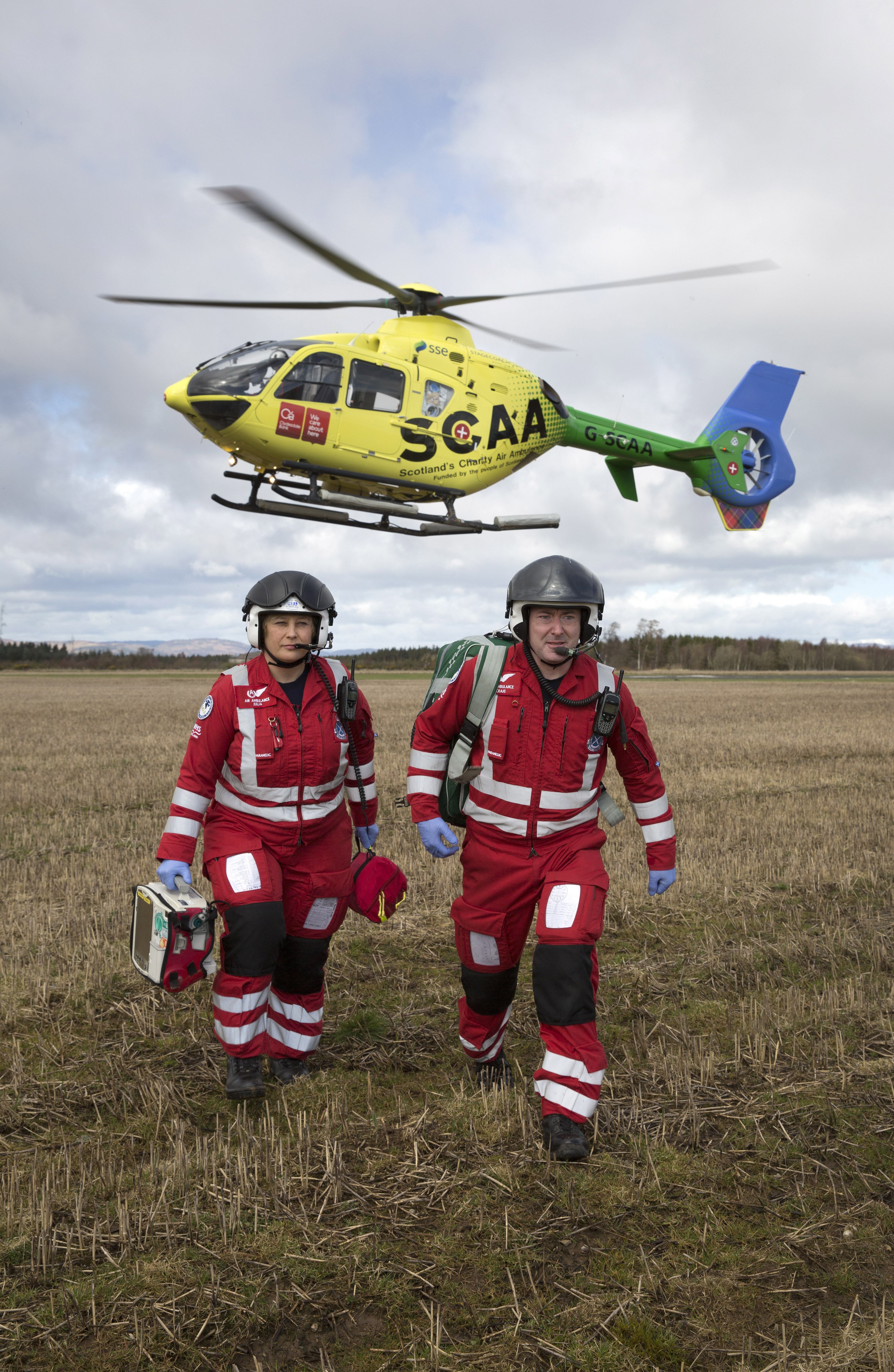 Two paramedics walk under helicopter.